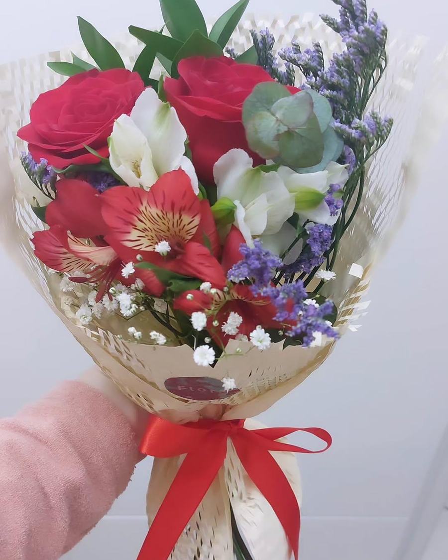 Buquê nº 01 — Ternura Vermelha: Rosas vermelhas e astromélias abraçadas por gipsofila e statice lilás, em papel kraft rendado com laço vermelho